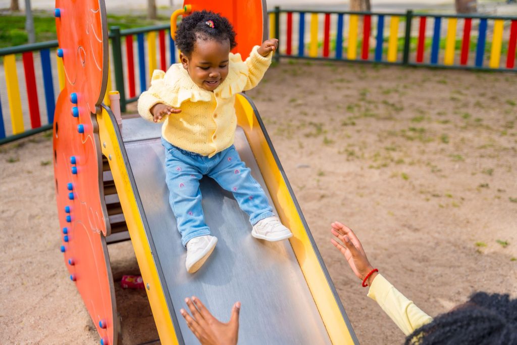 Little girl on a slide with the help of her mother while engaging in outdoor play ideas