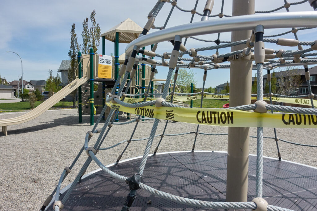 A playground with caution tape and a "Playground Closed" sign, indicating maintenance or restrictions.