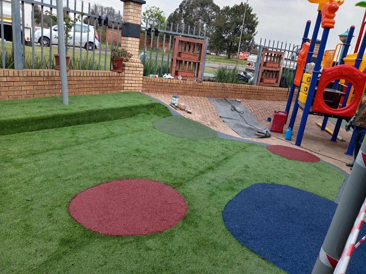Artificial grass with red and blue rubber circles around a creche jungle gym