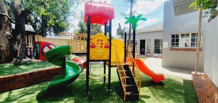 Jungle gym with a green spiral slide on artificial grass in a courtyard