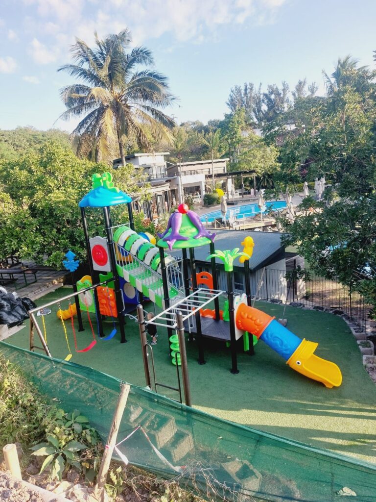 Jungle gym with monkey bars and tube slides on artificial grass in a garden with palm trees