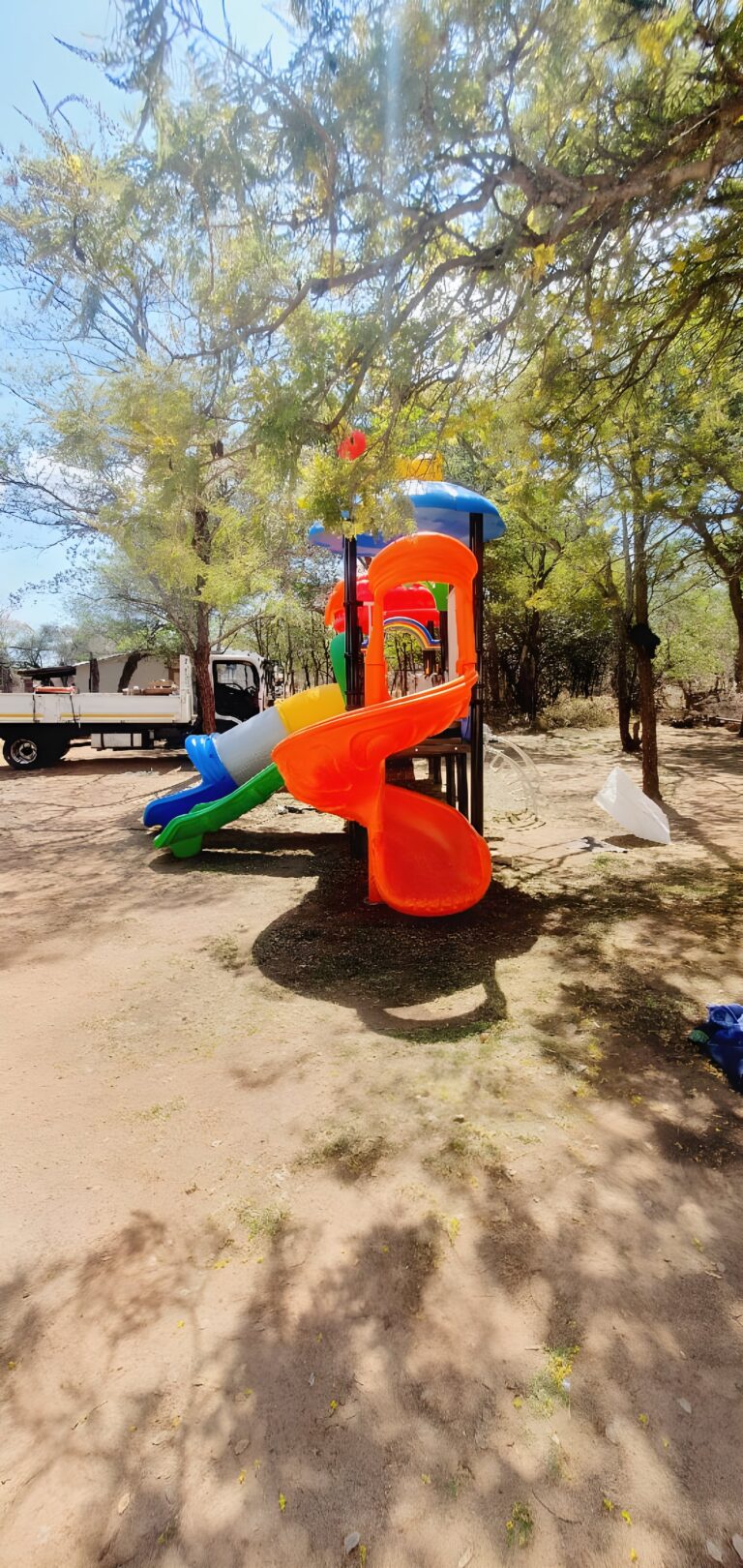 Jungle gym with an orange spiral slide under trees