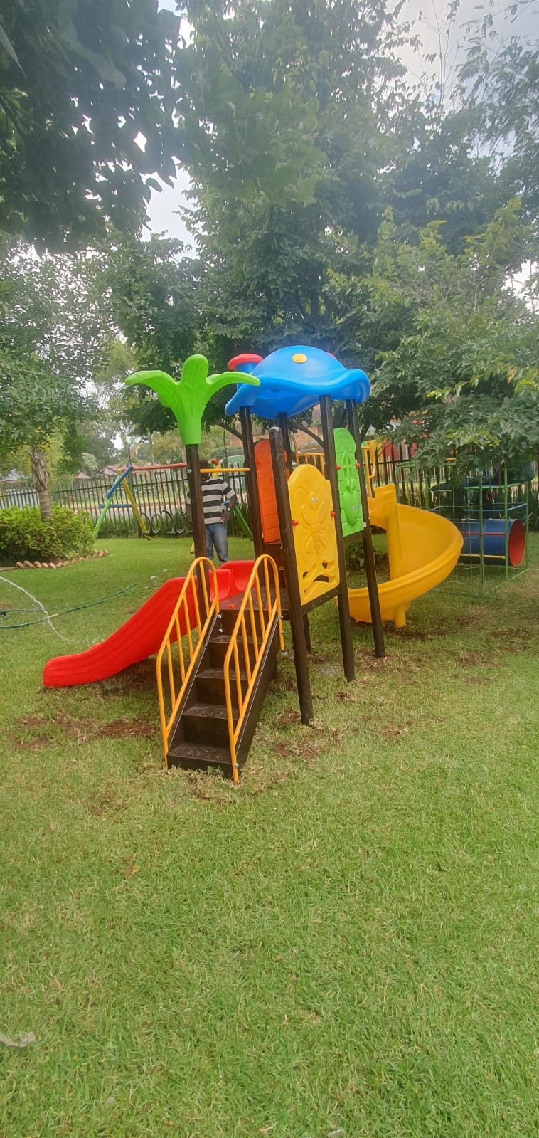 Jungle gym with a red slide and a yellow spiral slide on a lawn under trees