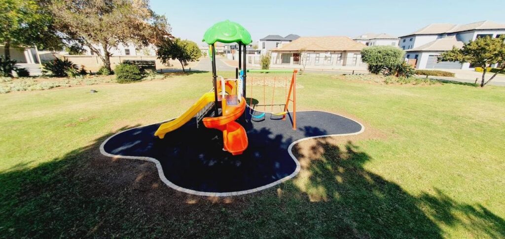 Small jungle gym on a black rubber wet pour island in a park lawn
