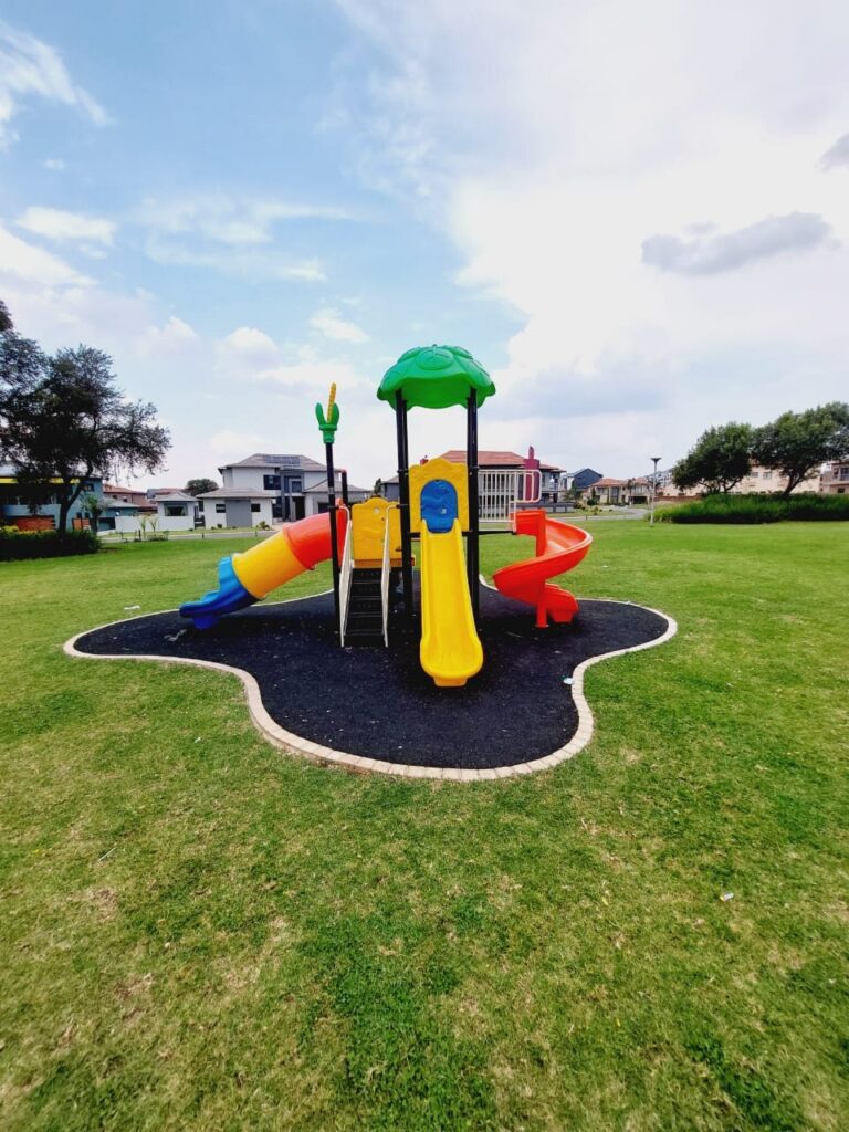 Jungle gym with a spiral slide on a black rubber wet pour island in a park lawn