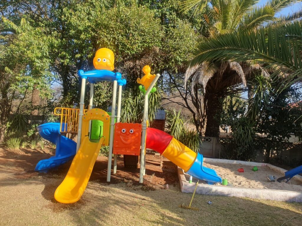 Jungle gym with spiral and tube slides beside a sandpit in a shaded garden