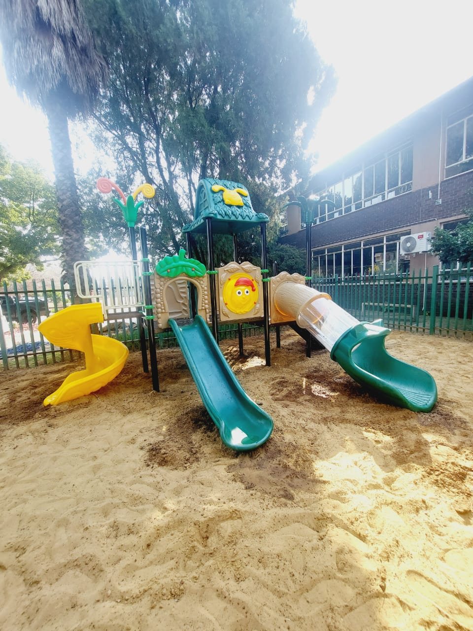 Jungle gym with three slides in a sand play area next to a school building