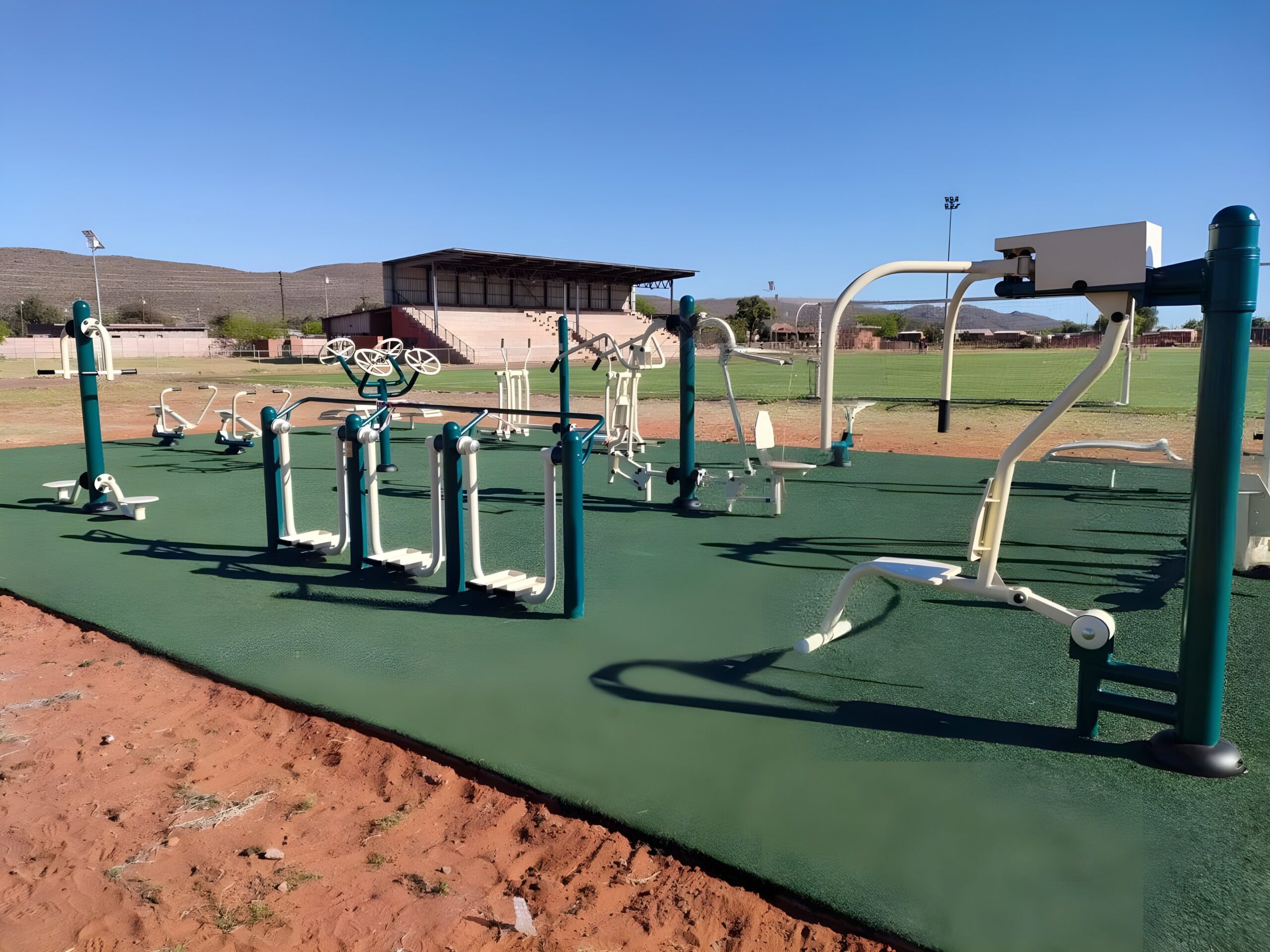 Outdoor gym equipment on green rubber safety surfacing at a sports field