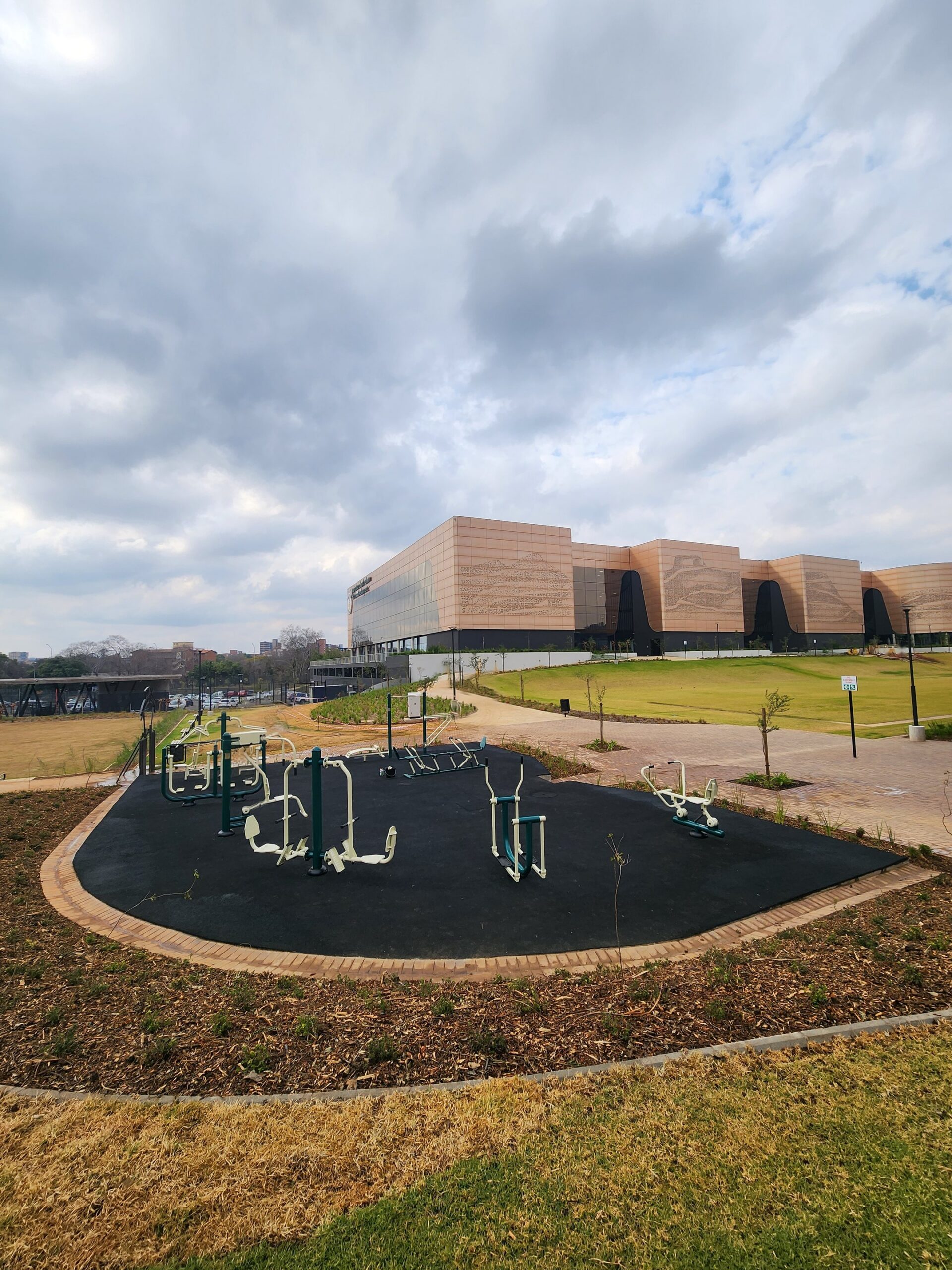 Outdoor gym stations on black rubber safety surfacing in a landscaped city park