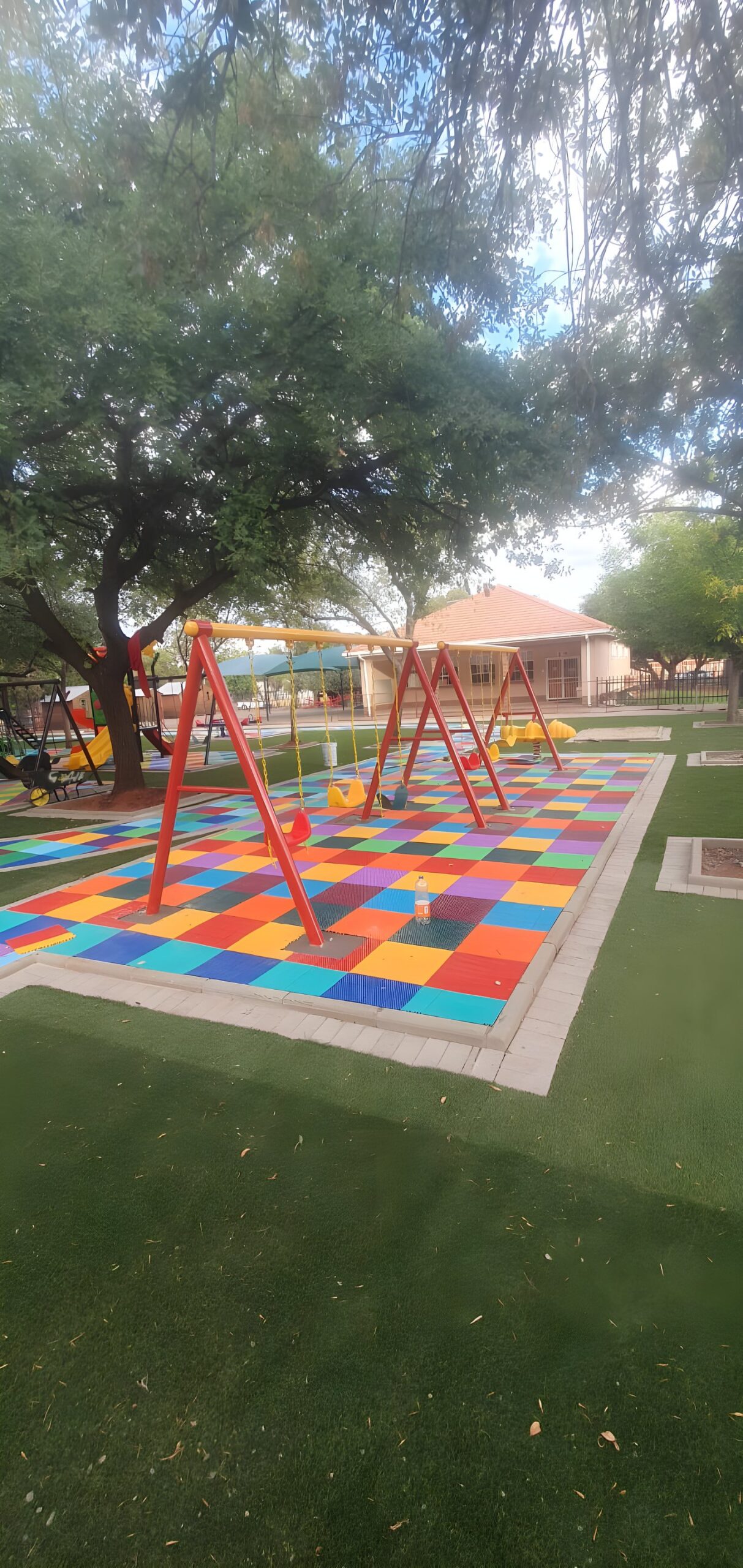 Red swing frames on multicoloured interlocking floor tiles surrounded by artificial grass