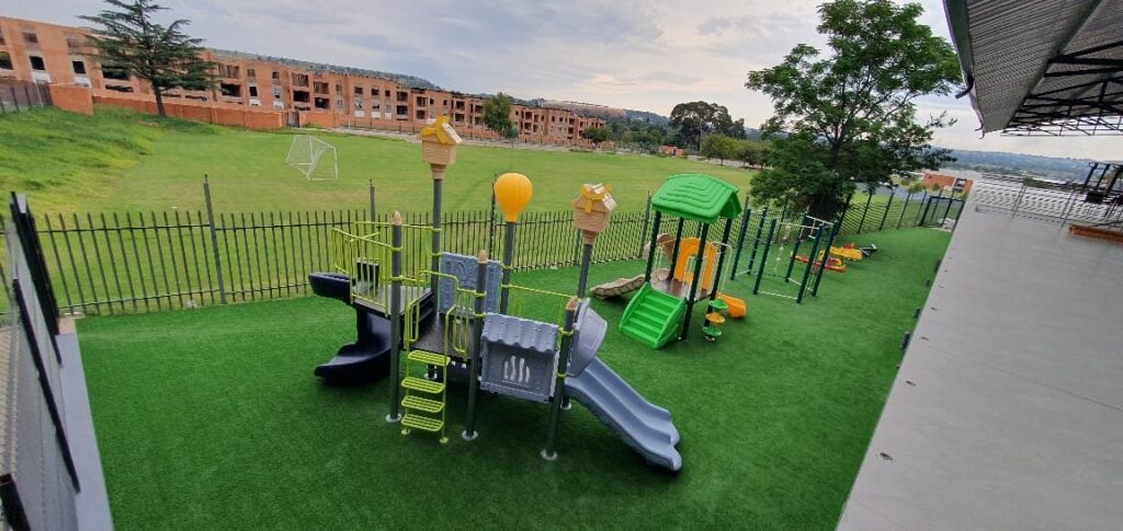 Jungle gym and a small playhouse on artificial grass next to a school sports field
