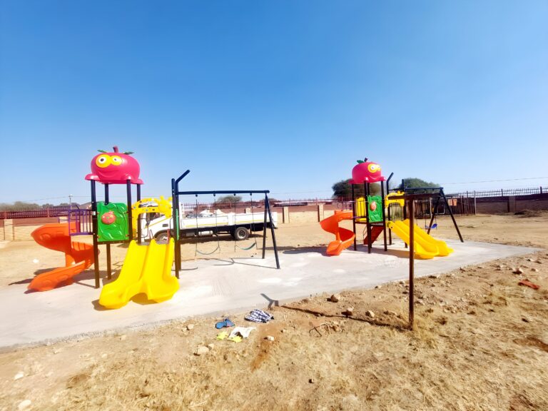 Two jungle gyms with spiral slides and a swing set on a concrete slab